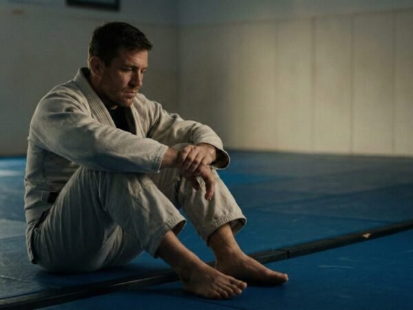 Faixa branca de jiu-jitsu treinando em aula supervisionada por instrutor em ambiente calmo